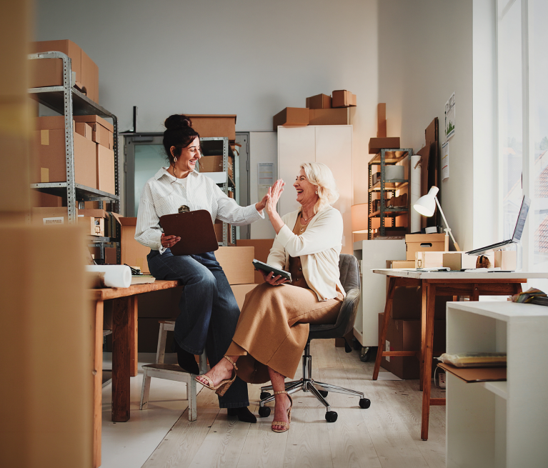 Female entrepreneurs in an online store's warehouse discussing business purchases with PragmaPay deferred payment